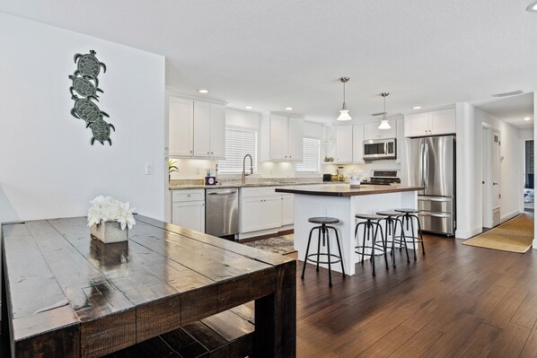 Una cocina moderna con armarios blancos, electrodomésticos de acero inoxidable y una mesa de comedor de madera con taburetes de bar.