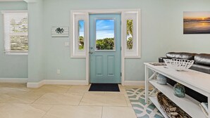 Un salon avec une porte de couleur turquoise, une console blanche agrémentée d’objets décoratifs et un canapé en cuir noir.