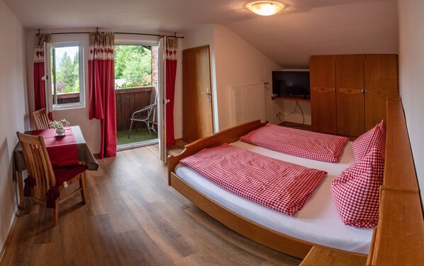 A bedroom with a wooden bed, a small table with a chair, and a TV mounted on the wall.