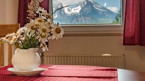 Une table ornée d’un vase de fleurs, recouverte d’une nappe rouge, et une fenêtre donnant sur une vue de montagne.