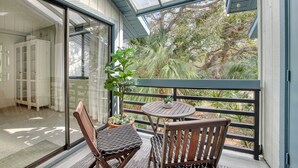 Ein Balkon mit Holzstuhl und Tisch, einem Blumentopf und Blick auf Bäume und Grün.