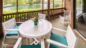 A covered patio with a round table and white chairs, overlooking a lake and greenery. - $150 activities - E-gift card when you book - Lakefront Screened in Porch | KLC 112 (Myrtle Beach)