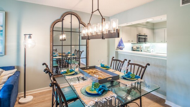 A dining area with a glass table, blue chairs, and a large mirror. - $150 activities - E-gift card when you book - Lakefront Screened in Porch | KLC 112 (Myrtle Beach)