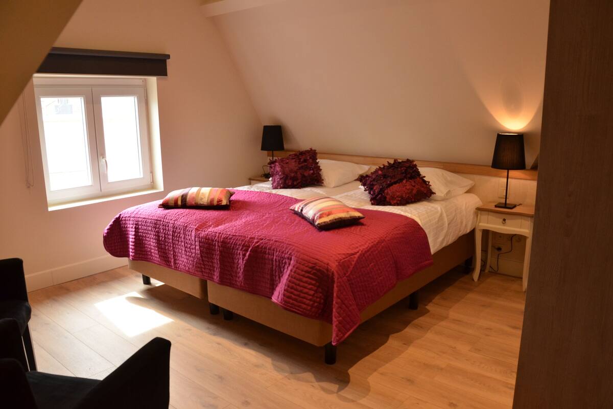 A bedroom with a bed, two bedside tables, a window, and a lamp.
