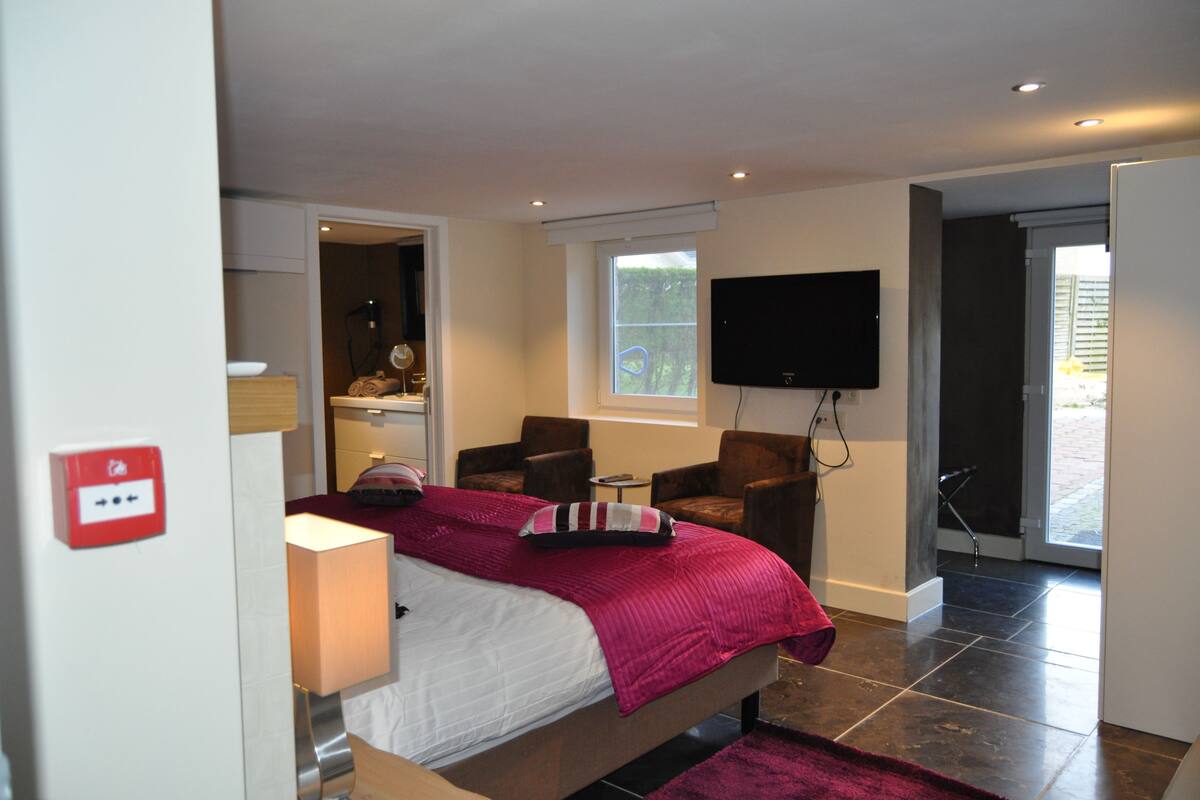 A bedroom with a bed, two chairs, a TV, and a window.