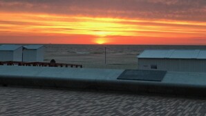 A sunset over the ocean with beach huts in the foreground. - Amylia (De Haan)