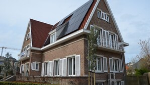 A two-story brick house with a steeply pitched roof, white shutters, and a balcony with white railings. - Amylia (De Haan)