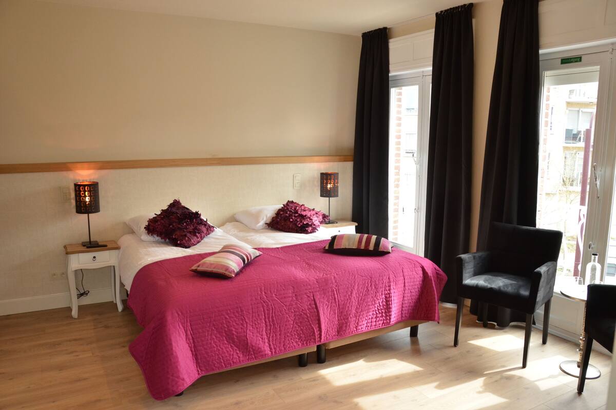 A hotel room with a bed, two bedside tables, a chair, and a window with curtains.
