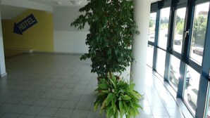 A lobby with a large potted plant, a sign indicating a hotel, and large windows with a view of the outside. - Sleep & Go Hotel Magdeburg (Magdeburg)