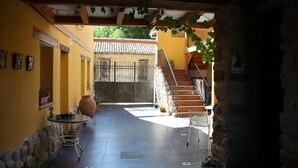 A courtyard with a tiled floor, a stone wall, a wooden staircase, and a metal gate. - CasaCándana (La Vecilla)