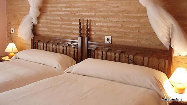A hotel room with two beds, a wooden headboard, and a brick wall. - CasaCándana (La Vecilla)