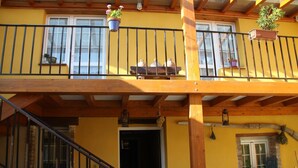 A yellow building with a wooden balcony, a staircase, and potted plants. - CasaCándana (La Vecilla)