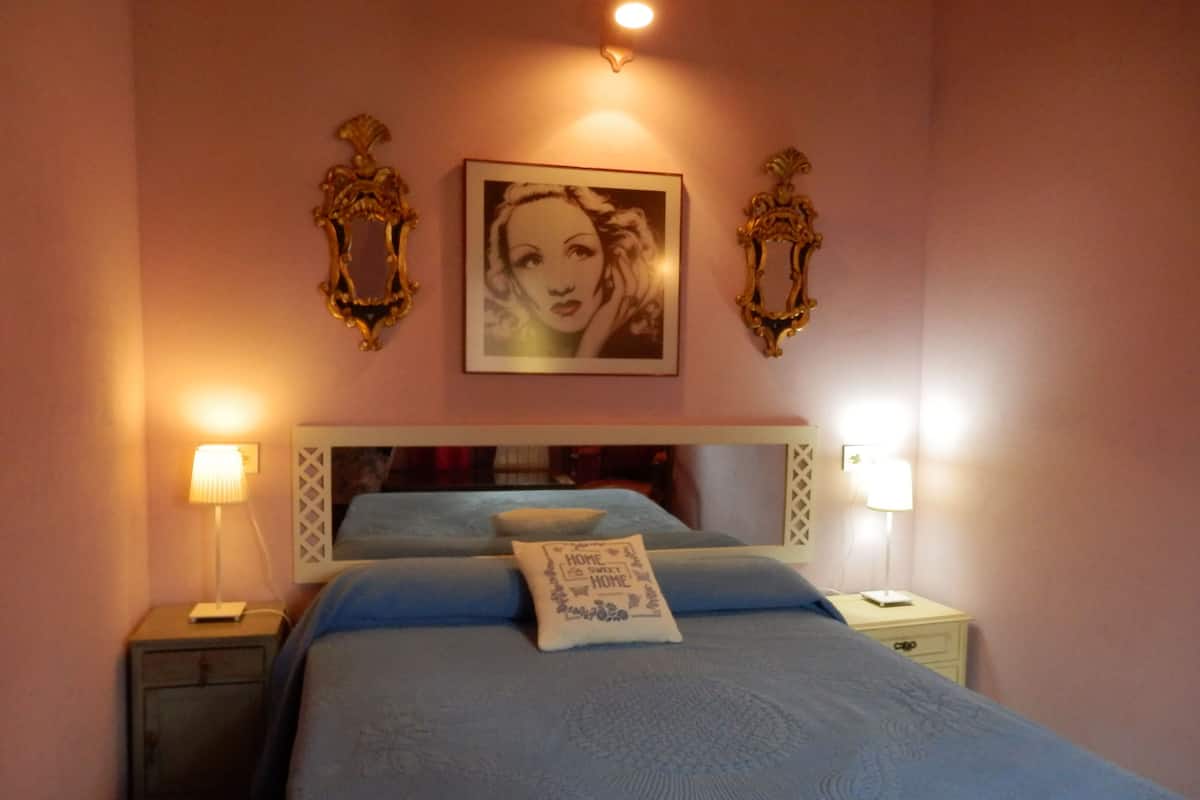 A bedroom with a bed, two bedside lamps, a nightstand, and a framed picture on the wall.