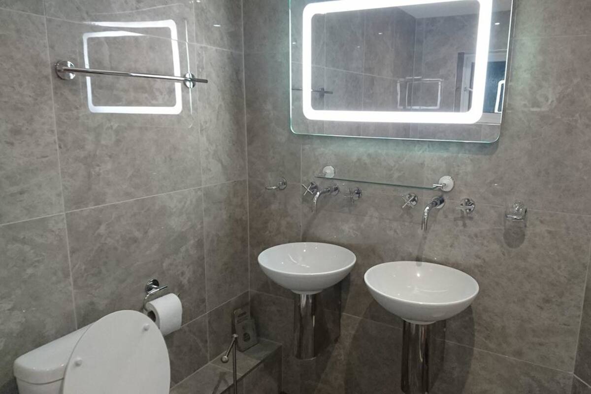 A modern bathroom with two sinks, a toilet, and a mirror with a light.