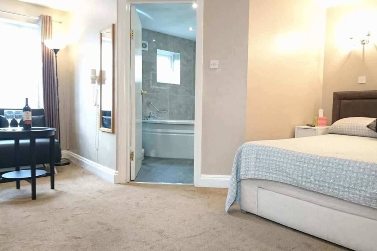 A hotel room with a bed, a desk with a chair, a bathroom with a shower and sink, and a view of the outside.