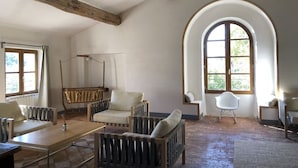 A spacious room with a high ceiling, wooden beams, a large arched window, and a swing chair.