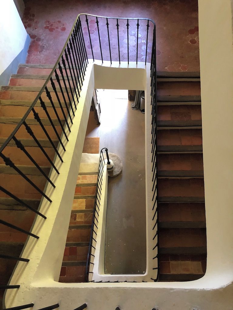Un escalier avec une rampe et une main courante en métal, menant à un palier doté d’un mur blanc et d’une fenêtre.