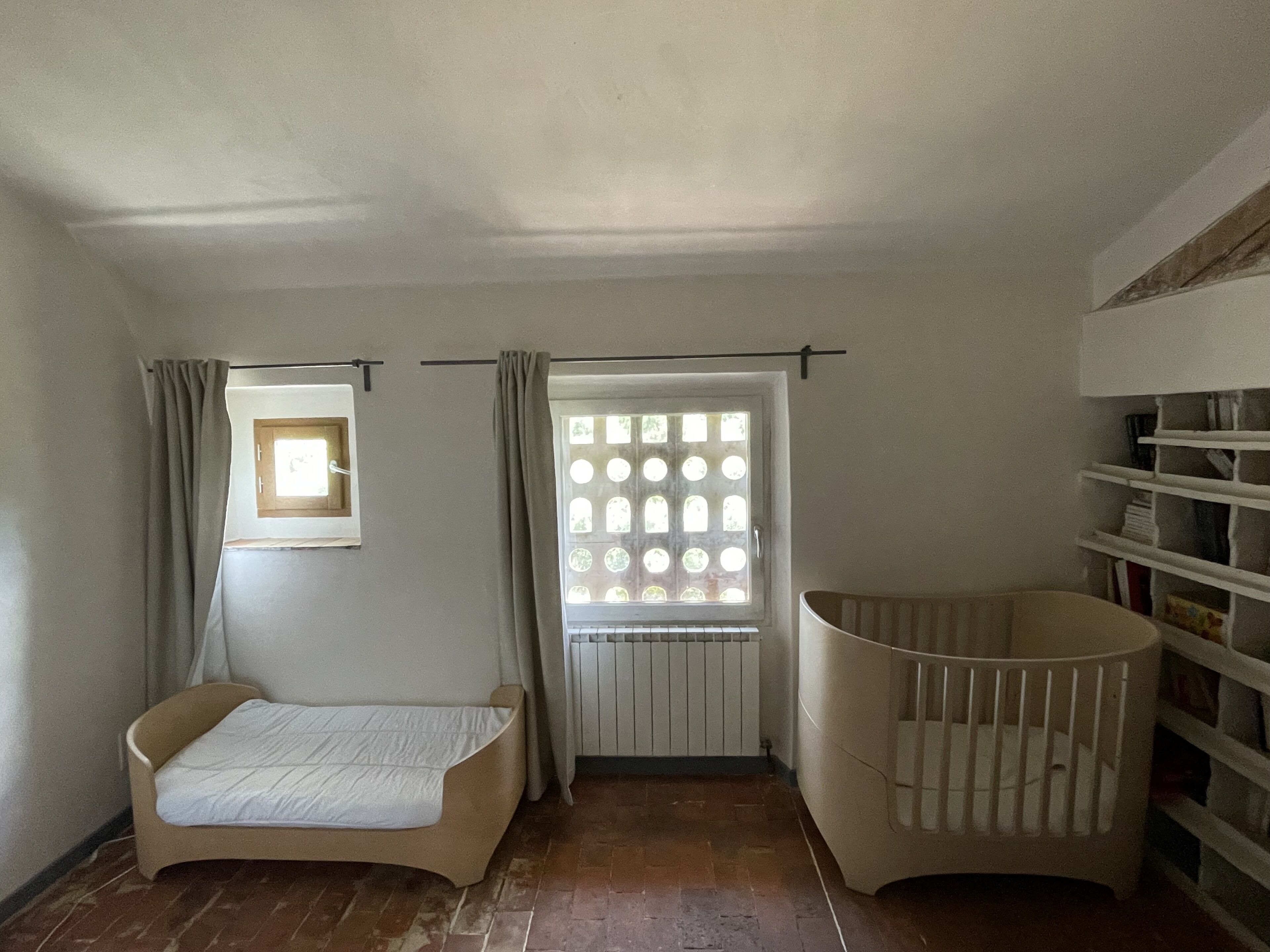 Een kamer met een bed, een ledikant, een raam met gordijnen en een radiator.