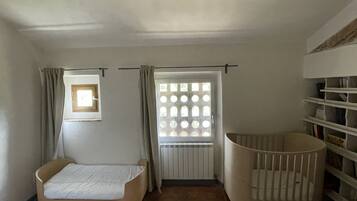 Een kamer met een bed, een ledikant, een raam met gordijnen en een radiator.
