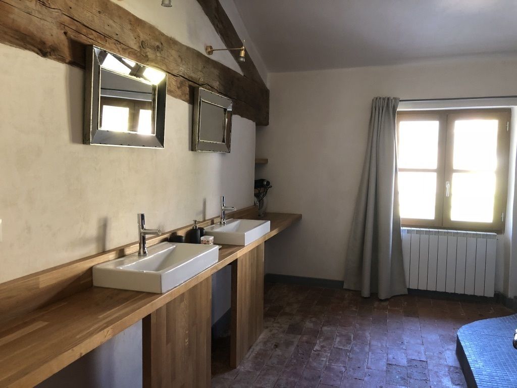 A bathroom with two sinks, wooden vanity, large mirror, and a window with curtains.