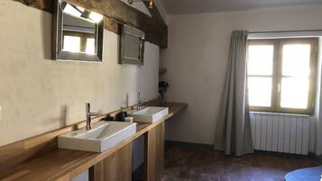 A bathroom with two sinks, wooden vanity, large mirror, and a window with curtains.