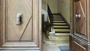 A wooden door with a lion head knocker, a staircase with a black railing, and a potted plant on the landing.
