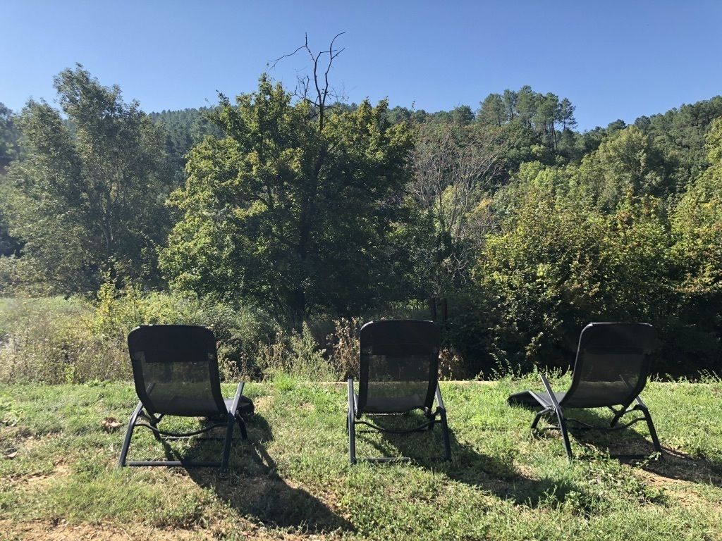 Tres sillas al aire libre en un área con césped y árboles al fondo.