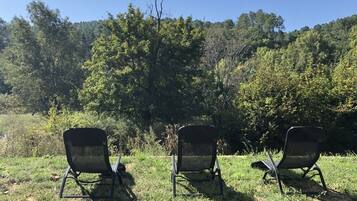 Tres sillas al aire libre en un área con césped y árboles al fondo.