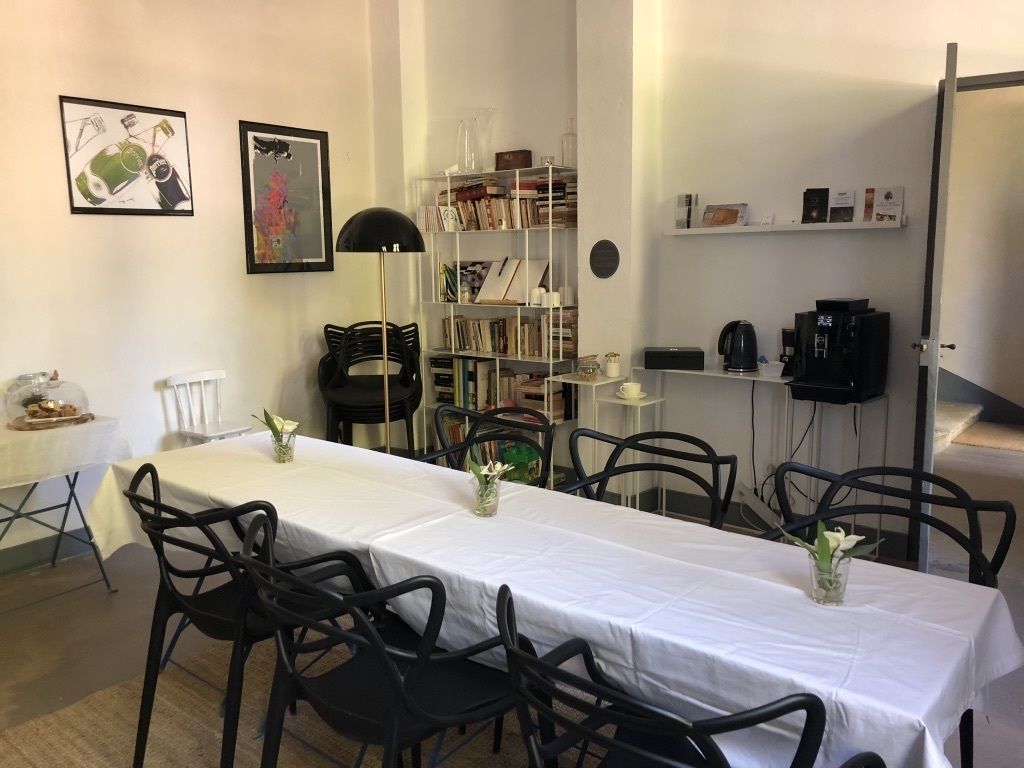 Et spiseområde med et langt bord, sorte stole, en bogreol og en kaffemaskine.