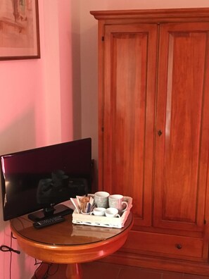 A room with a wooden cabinet, a television on a stand, and a small table with a tray holding cups and a remote control. - Affittacamere Villa Bagno Santo (Manciano)