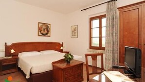 A bedroom with a wooden bed, bedside tables, a desk with a computer, a chair, and a window with curtains. - Affittacamere Villa Bagno Santo (Manciano)