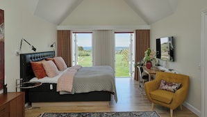 Un dormitorio con una cama grande, un sillón amarillo, un escritorio con una silla y vistas al exterior a través de una puerta corredera.