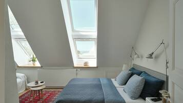 A bedroom with a bed, bedside table, lamp, and a view through a skylight.