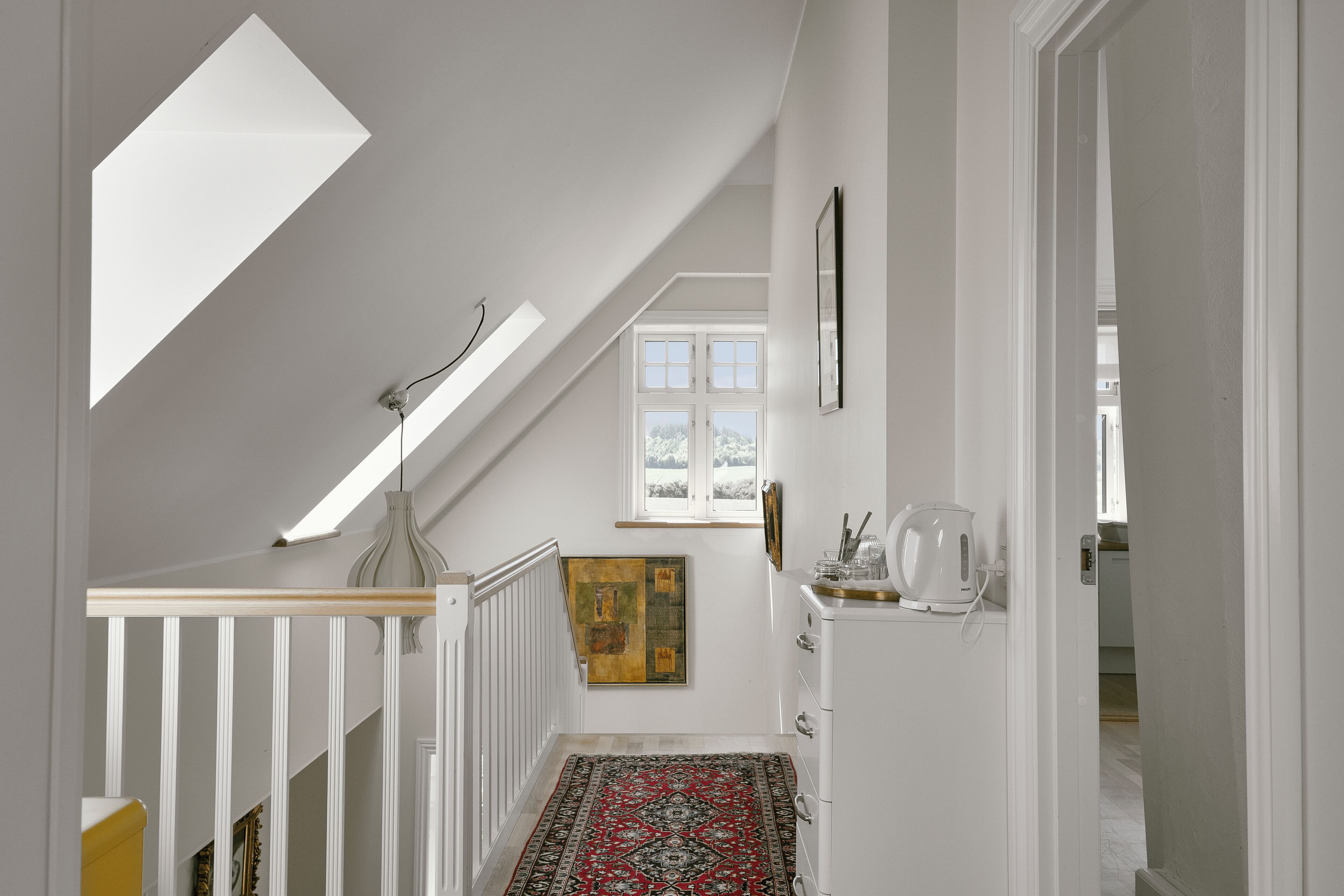 A staircase with a skylight, a patterned rug, and a painting on the wall.
