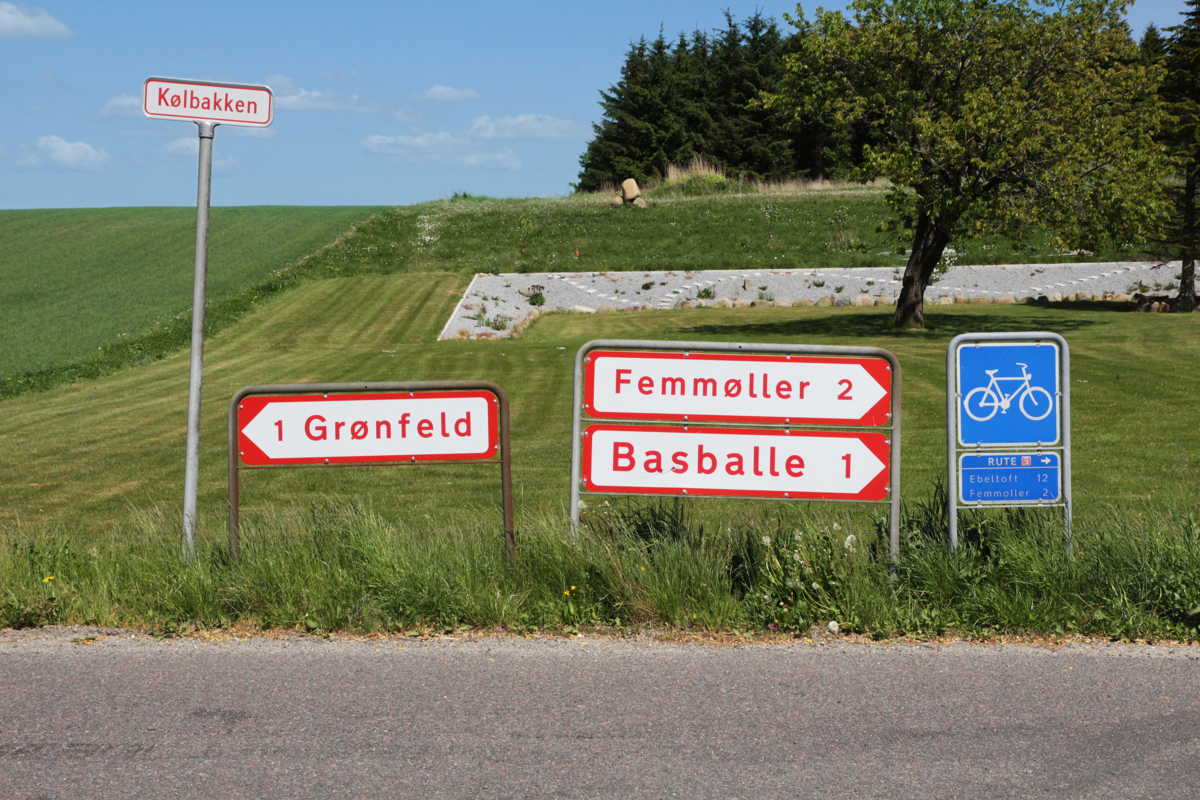 Directional signs for Gronfeld, Femmöller, and Basballe, and a bike route sign.