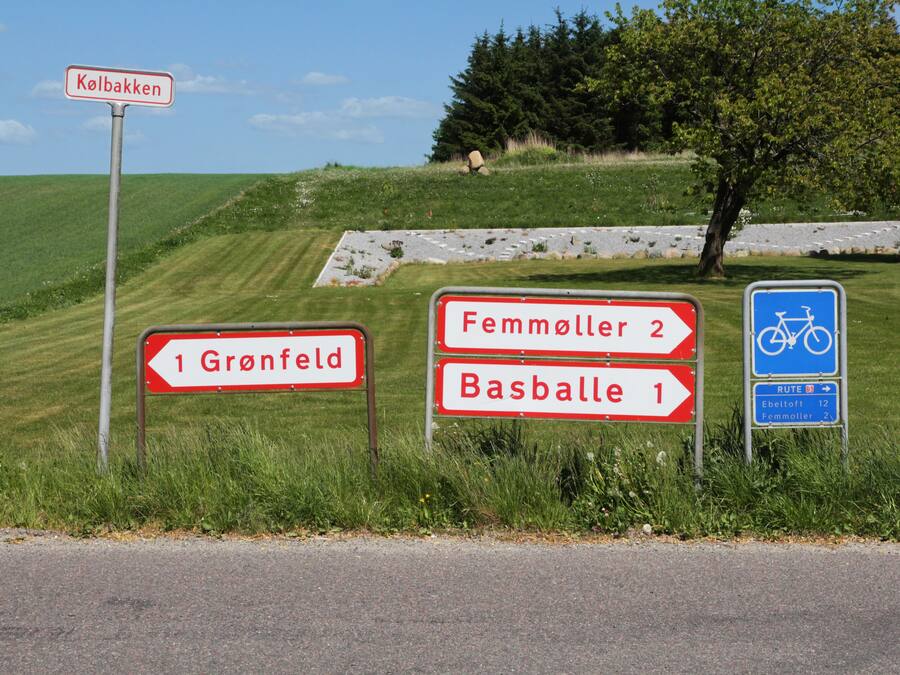 Directional signs for Gronfeld, Femmöller, and Basballe, and a bike route sign.