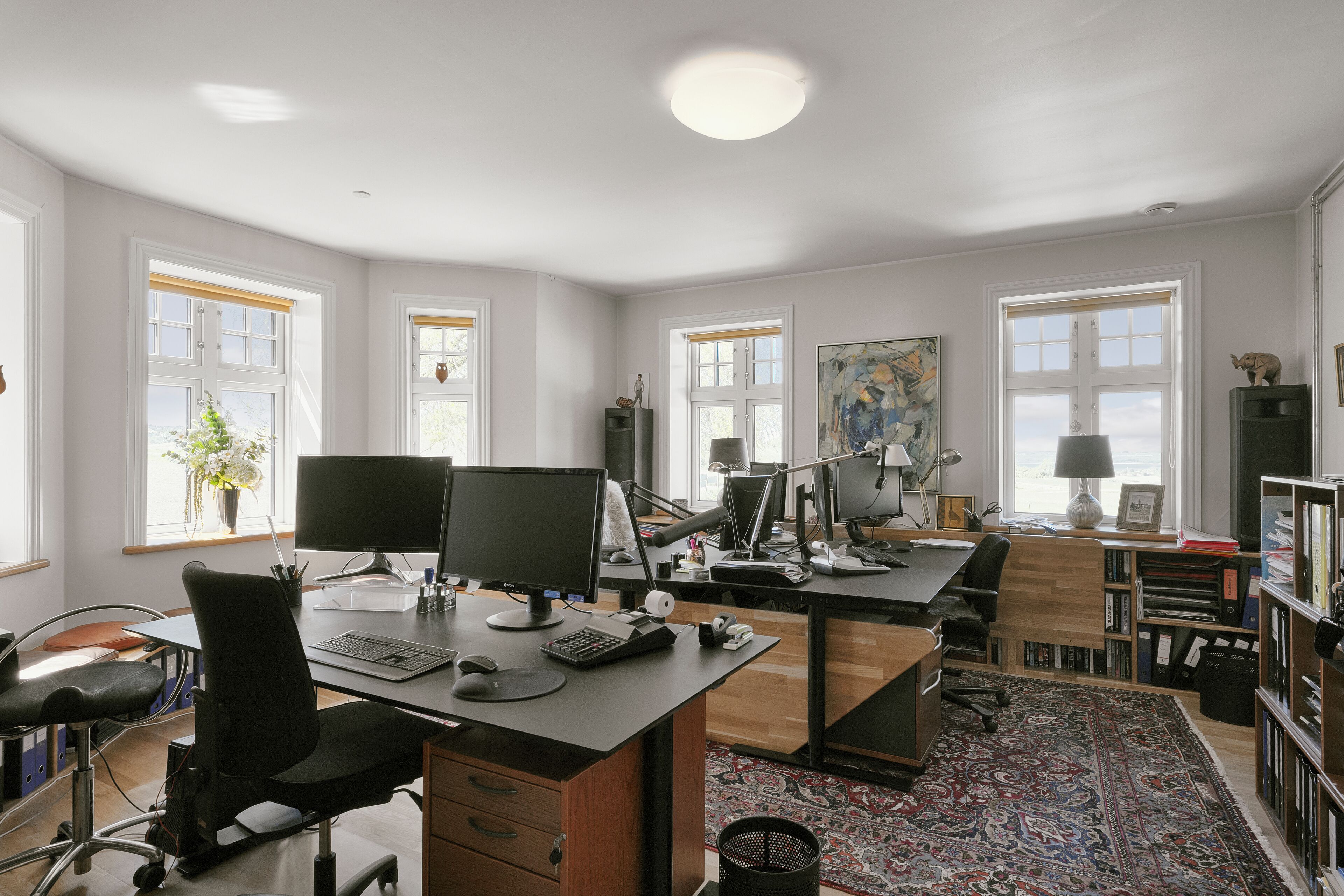 A modern office with multiple desks, computers, and a large bookshelf.