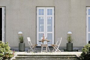 En terrasse med et bord, stole, en flaske og to krukker med planter.