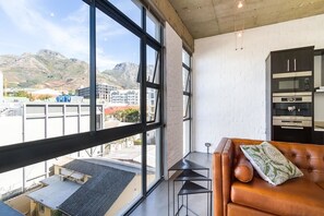 A modern interior with a large window, a leather sofa, and a kitchen area. - Temple House (Cape Town)