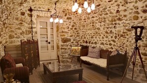 Una habitación acogedora con pared de piedra, sofá de madera, mesa de centro de vidrio y un trípode.