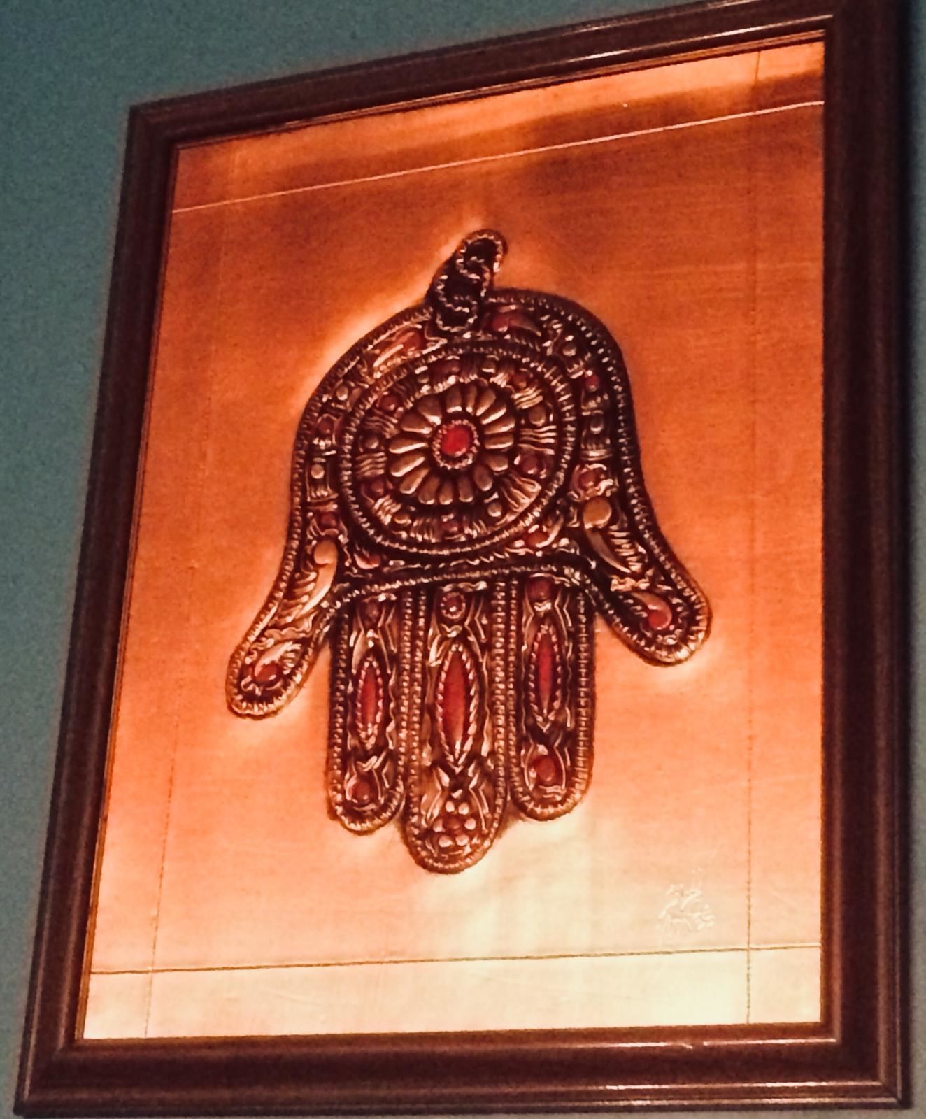 A framed hand symbol with intricate designs and a central red gem.