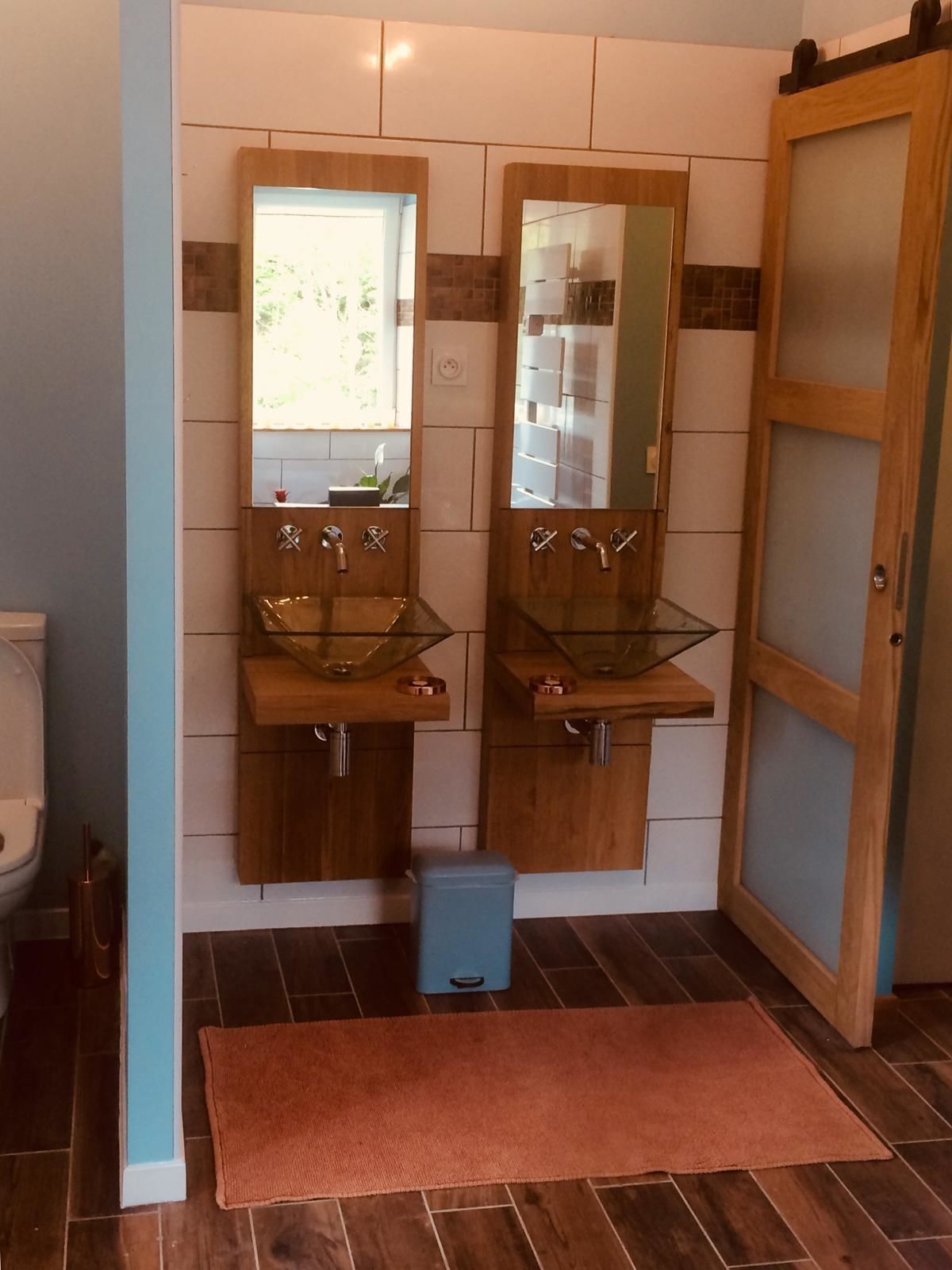 A bathroom with two glass sinks, a toilet, and a blue trash bin.