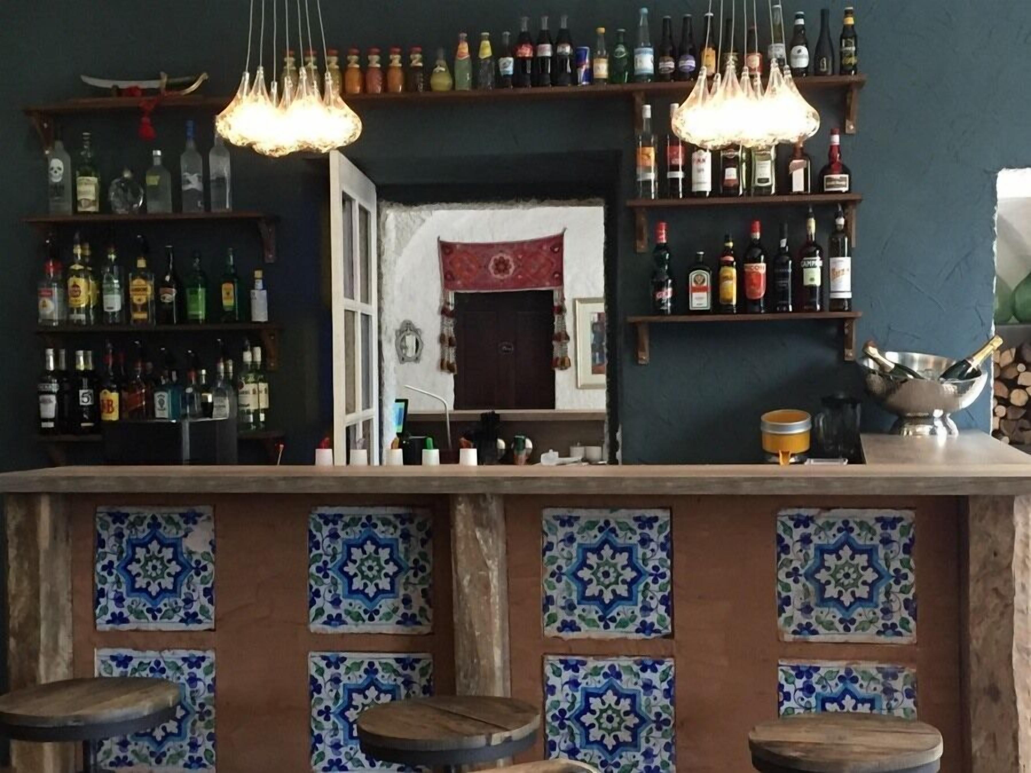 A bar area with shelves of liquor bottles, hanging light fixtures, and patterned tiles.