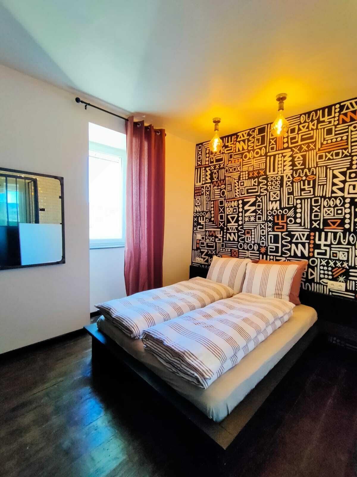 Ein Schlafzimmer mit Bett, Wand mit Muster und Fenster mit Vorhängen.