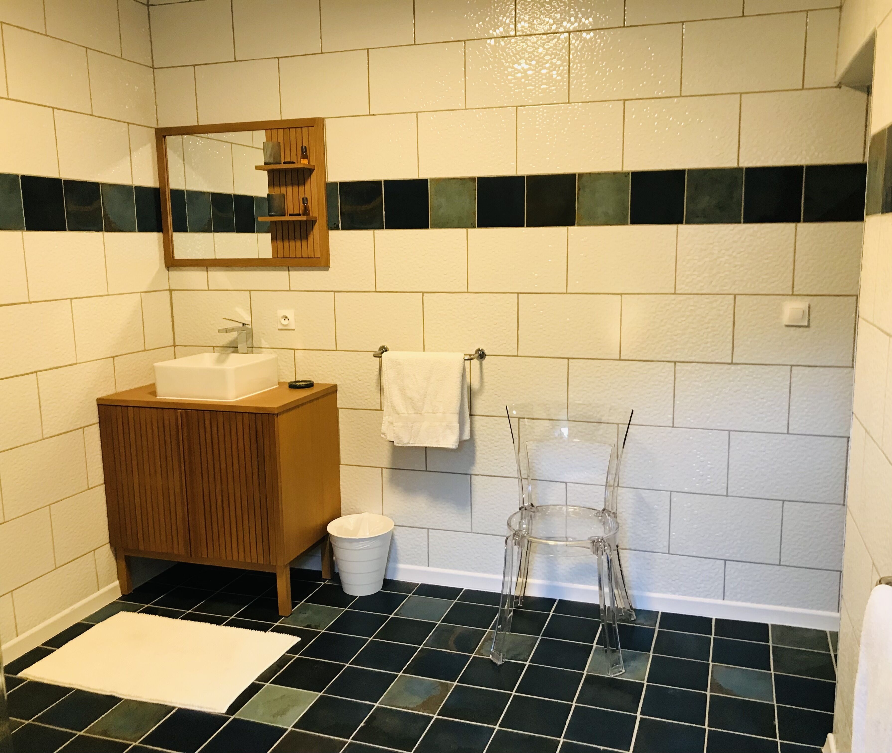 Een badkamer met een wit wastafel, houten wastafelmeubel, zwart-wit betegelde vloer en een spiegel boven het wastafel.