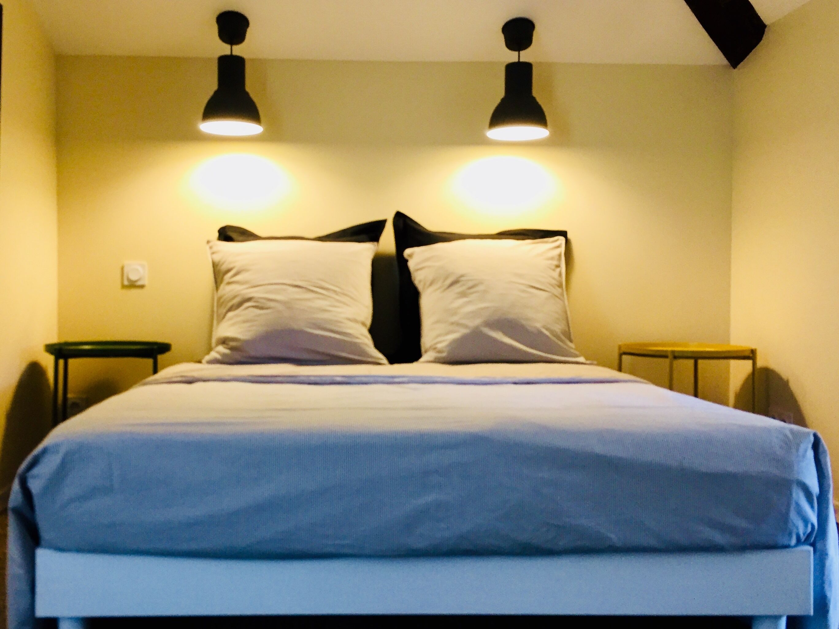 A bed with a white and blue bedspread, two black nightstands, and two pendant lights on the ceiling.