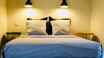 A bed with a white and blue bedspread, two black nightstands, and two pendant lights on the ceiling.