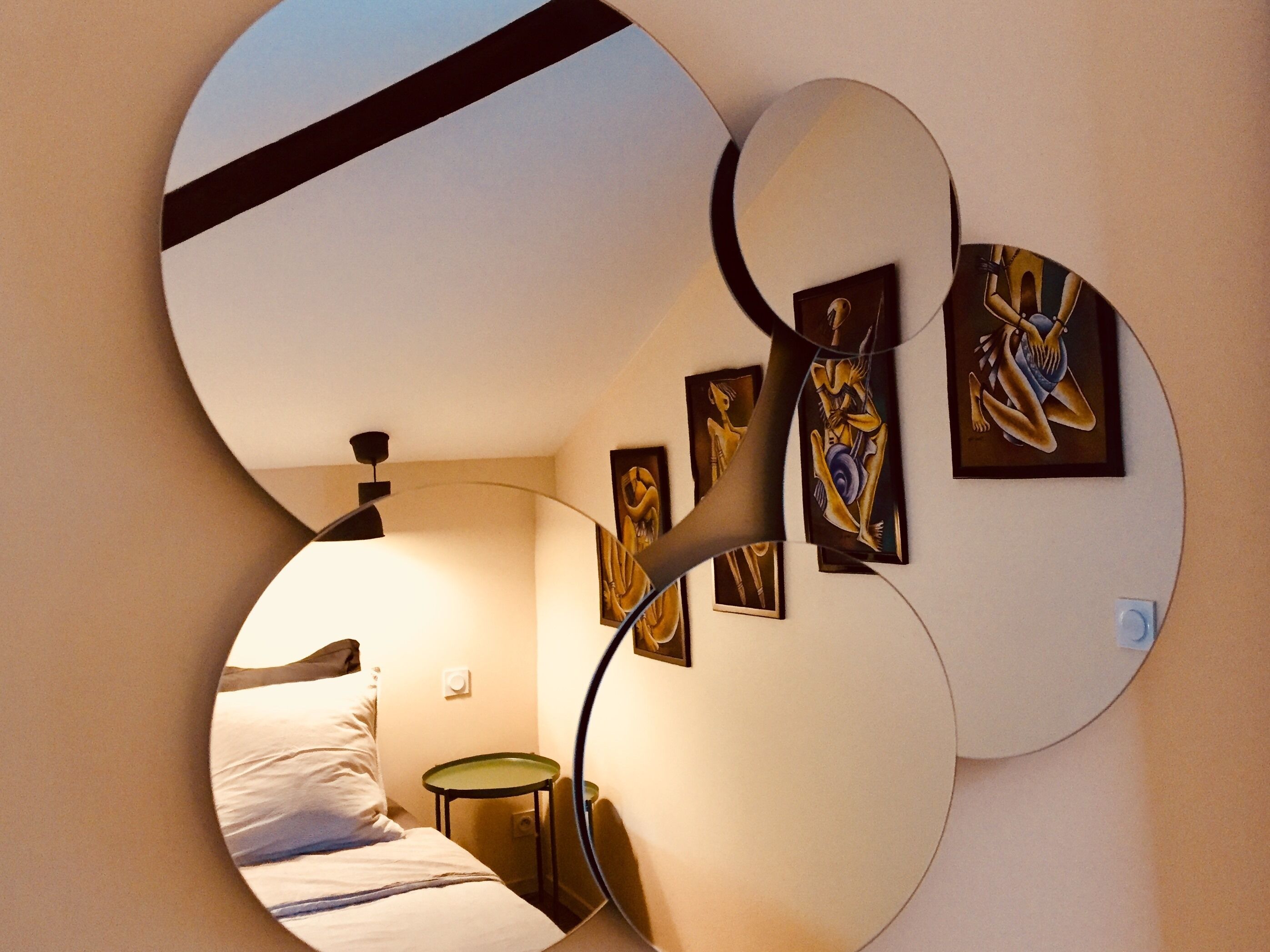 A circular mirror reflecting a bedroom with a bed, a nightstand, and wall art.