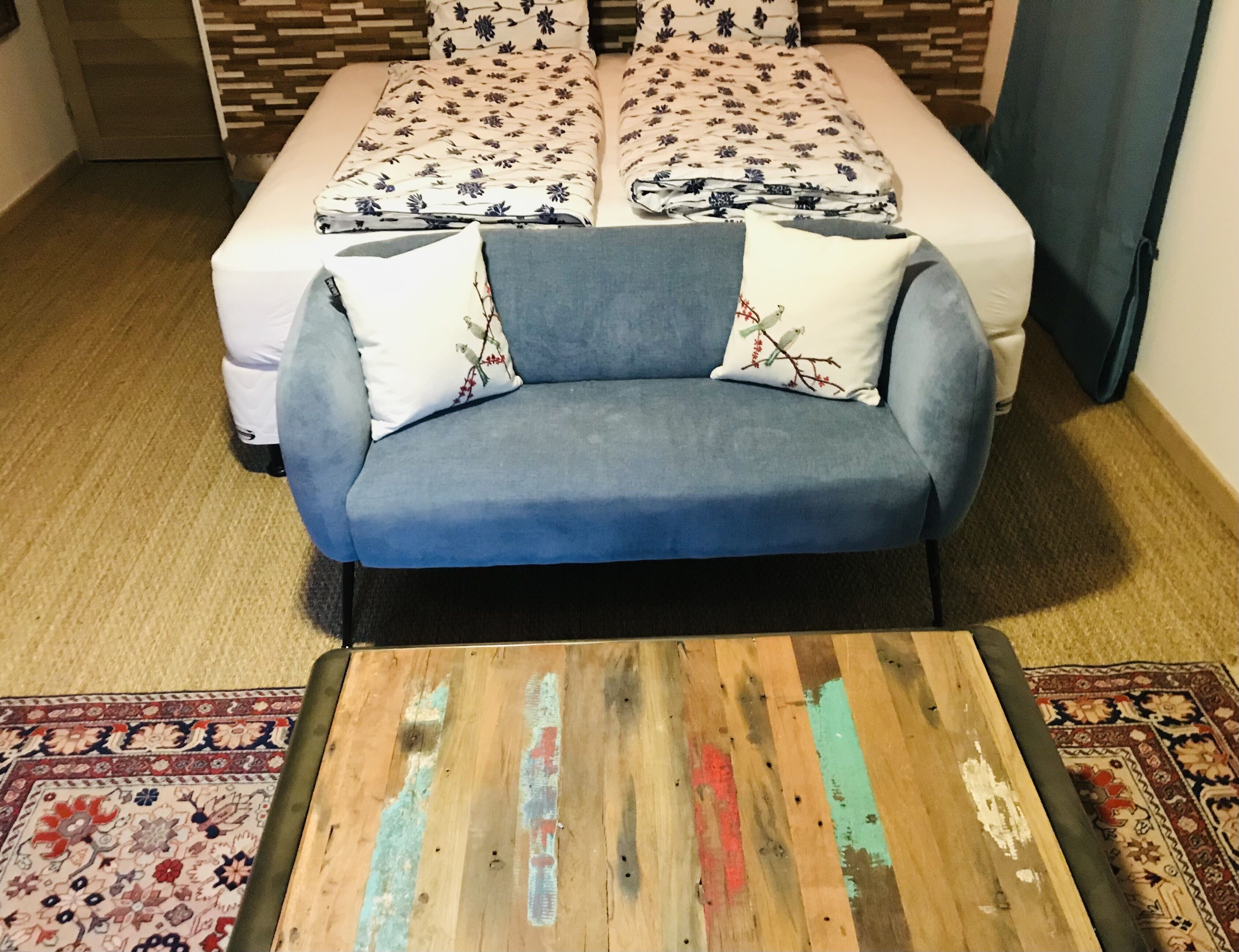 Una habitación con un sofá azul, una mesa de centro de madera y una alfombra estampada.