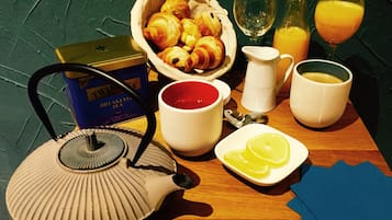 Una mesa de desayuno con cruasanes, una tetera, tazas y vasos de jugo de naranja.